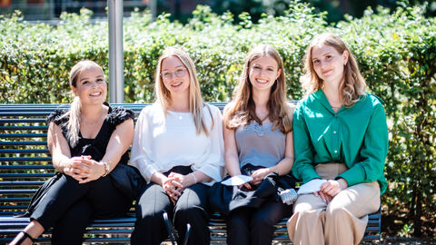 Vier Anwärterinnen sitzen auf einer Bank und lachen in die Kamera