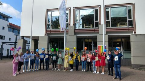 Diversity-Tag 2022 Mehrere Personen, bunt gekleidet und in der Reihenflge eines Regenbogen stehen mit Schildern und Luftballons in der Hand vor einem Finanzamtsgebäude. Die Schilder schreiben den Text Diversity 2022.