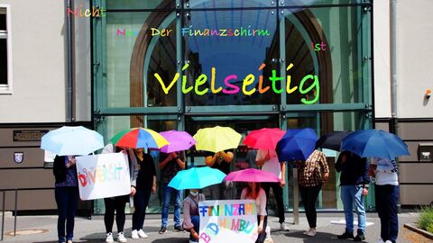 Anwärter*innen aus dem Finanzamt Bad Hombrug stehen mit bunten Schirmen vor dem Finanzamtsgebäude. Darüber liegt der Schriftzug "Nicht nur der Finanzschirm ist vielseitig".
