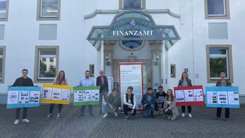 Personen stehen mit gebastelten Plakaten (Reiseführer) vor dem Finanzamt Rheingau-Taunus