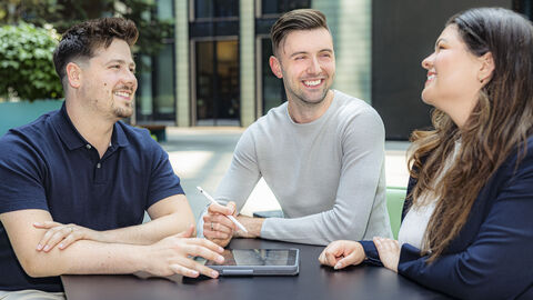 Drei Personen sitzen am Tisch und lachen.